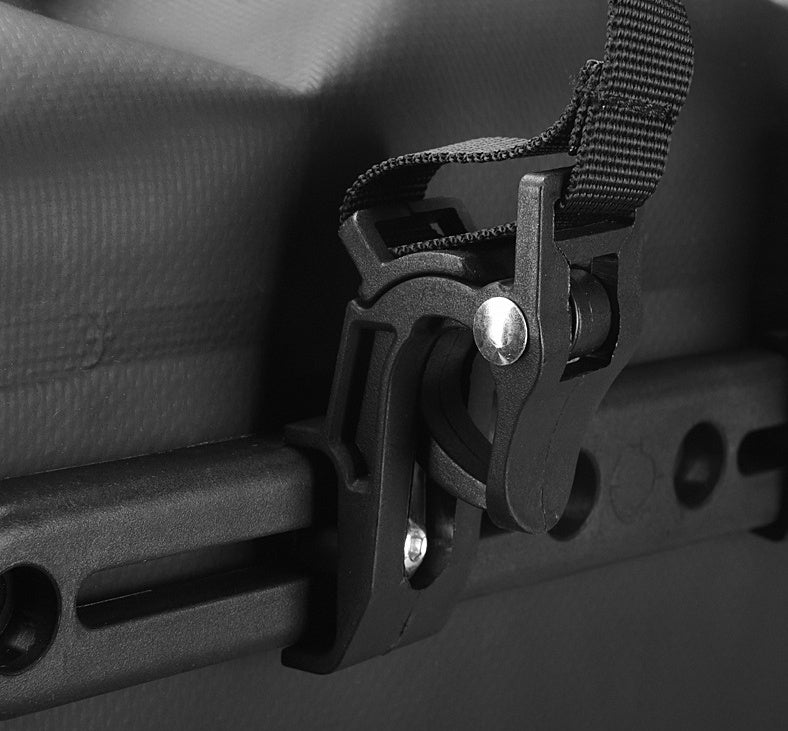 Close-up of a black bicycle pannier attachment clip on a dark background