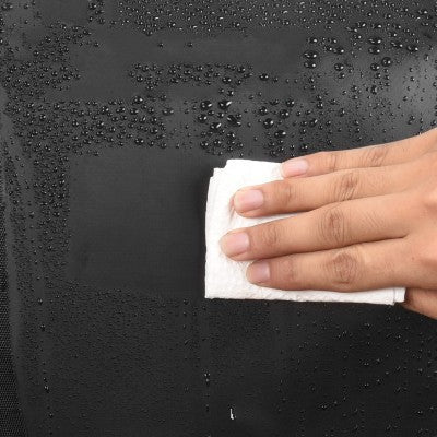 Hand using a white cloth to wipe a black bicycle pannier with water droplets.