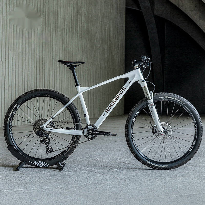 White mountain bike mounted in a wheel stand with 'RockBros' branding on a concrete floor.
