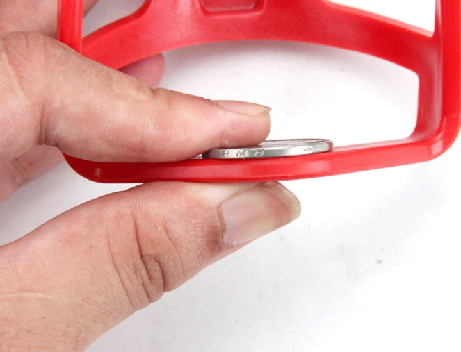 Hand holding a red Bicycle Bottle Holder/Cage with a coin inside on a white background
