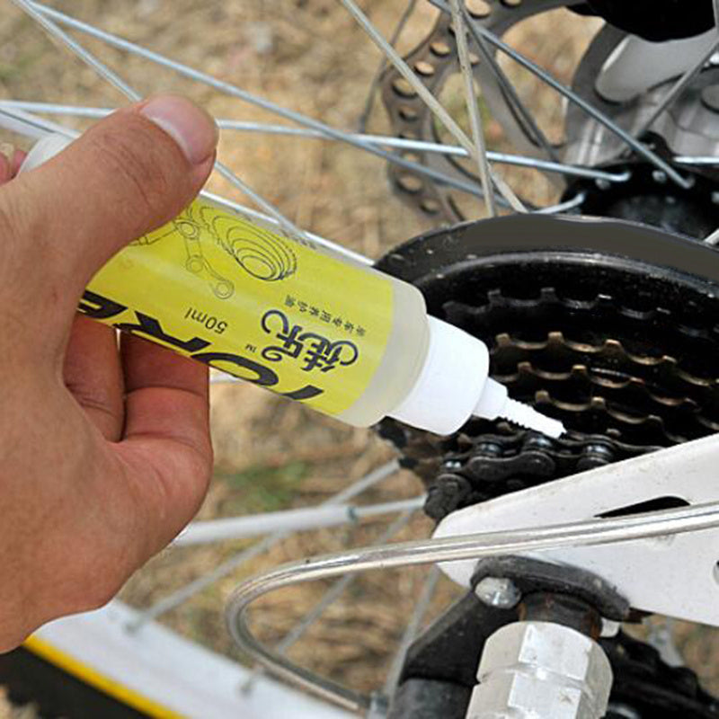 Hand applying a yellow lubricant bottle to a bicycle chain