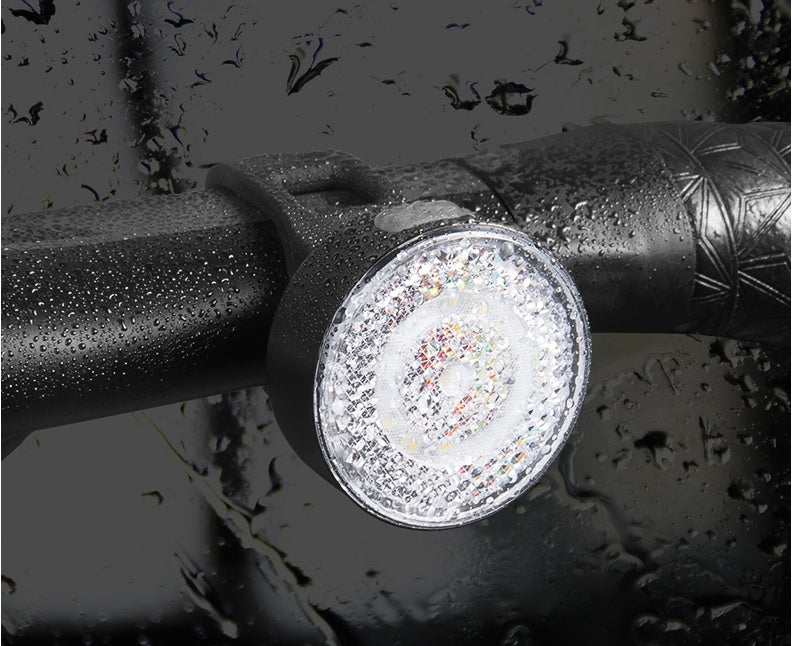 Close-up of a round reflective light on a bicycle handlebar with water droplets.