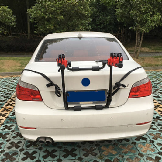 Car with a bike rack attached to the back, parked on a patterned surface with greenery in the background.