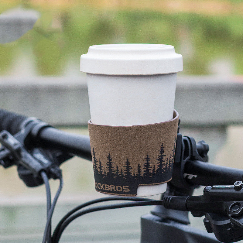 White coffee cup with a brown sleeve in a cup holder mounted on a bicycle handlebar, blurred green background