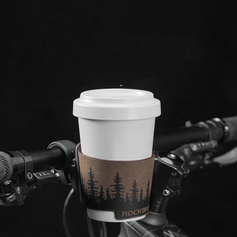 White coffee cup with a brown cup holder mounted on a bicycle handlebar against a black background