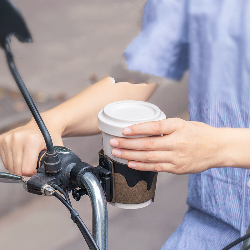 Person holding a coffee cup in a cup holder attached to a bicycle handlebar