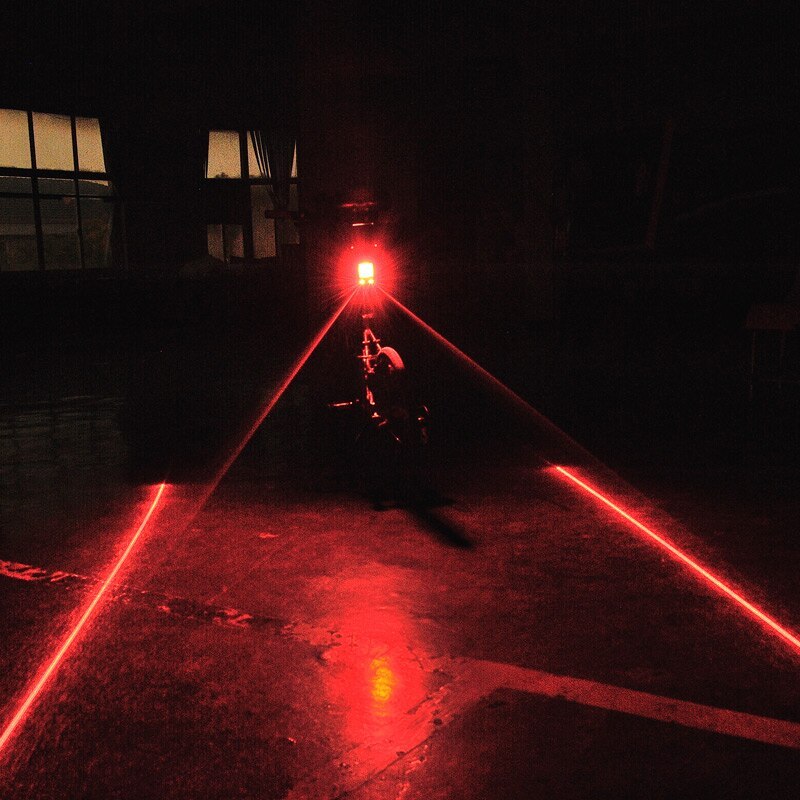 Red laser beams emitted by a LED Bicycle Indicator Light on a dark floor with a building in the background