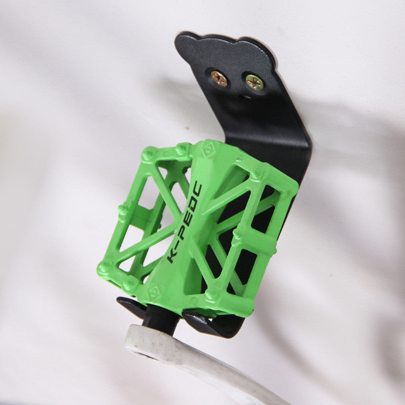 Black metal bicycle storage hook supporting a green pedal on a white background