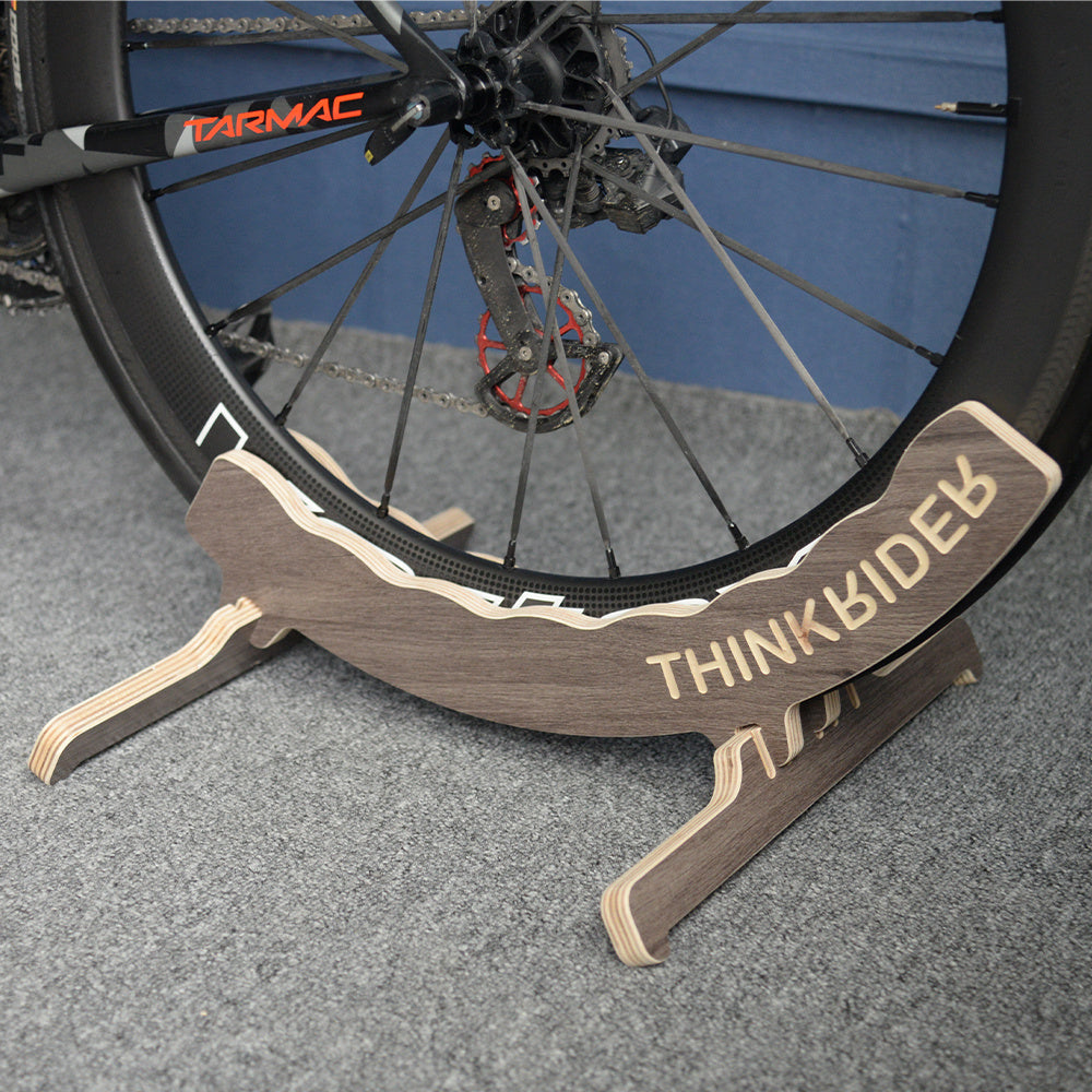 Bicycle wheel with a wooden THINKRIDER stand on a gray surface
