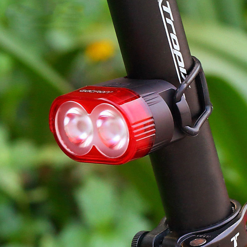 Red bicycle light attached to a black bike frame with a blurred green background