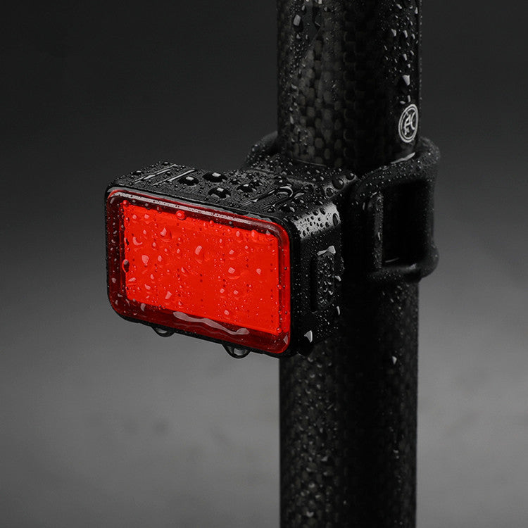 Red bicycle tail light attached to a black seatpost with water droplets on a dark background