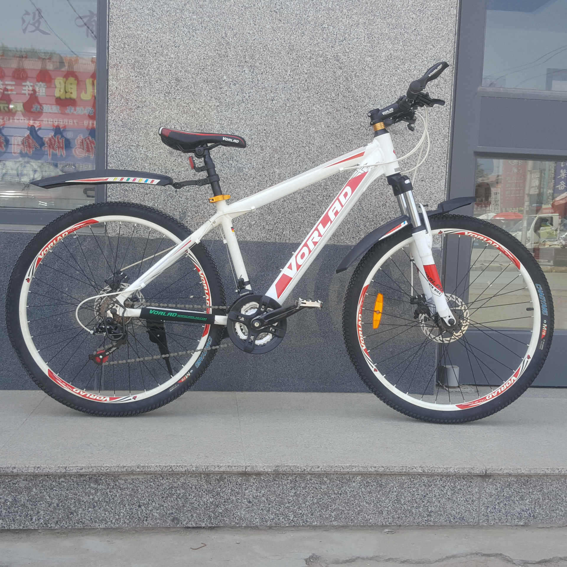 White bicycle with red and black details and front and rear detachable mudguards on a concrete surface.