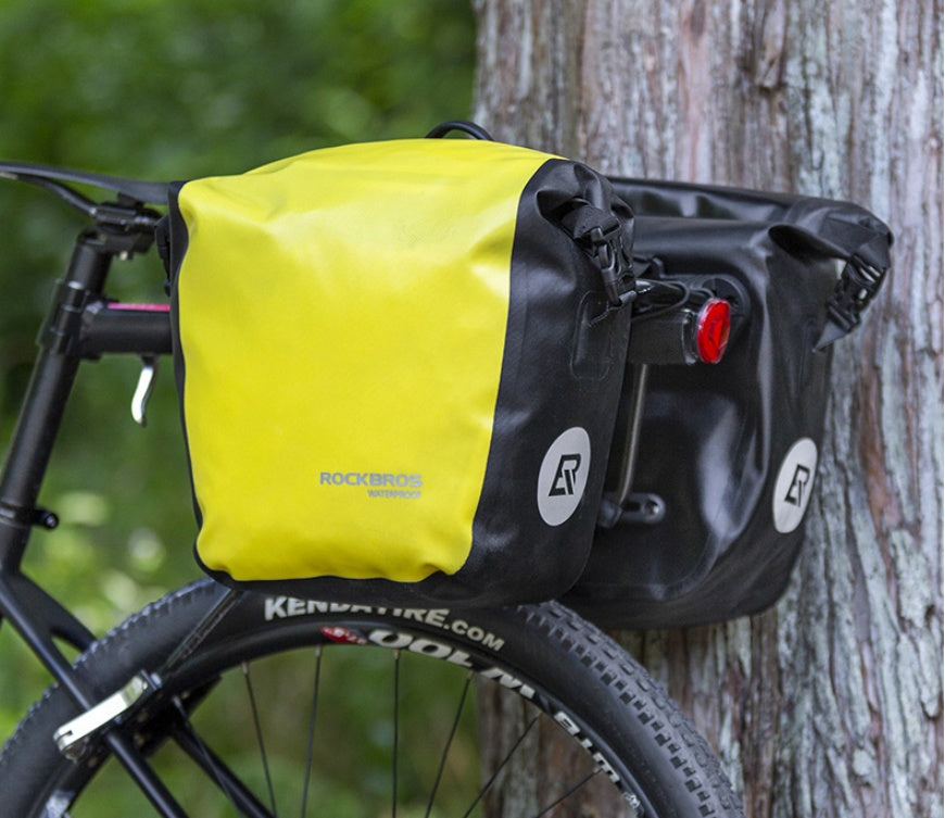 Yellow and black Waterproof Bicycle Bag / Pannier attached to a bicycle against a tree.