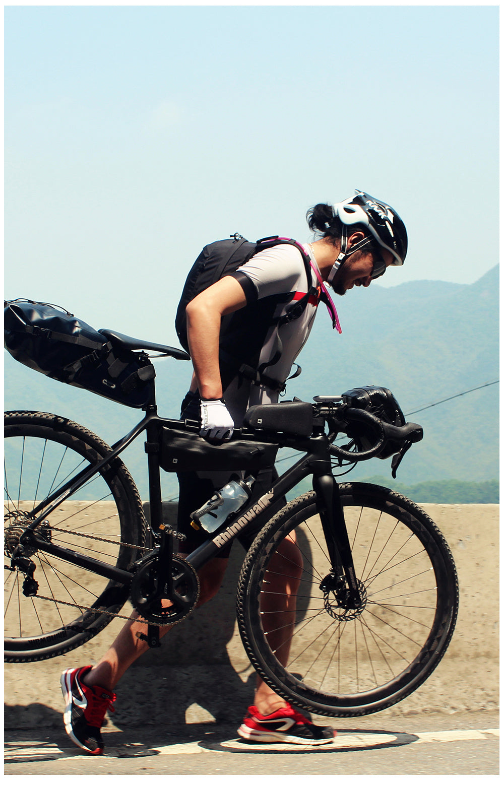 Person with a bicycle on a road with a Waterproof Bicycle Frame Bag with mountains in the background